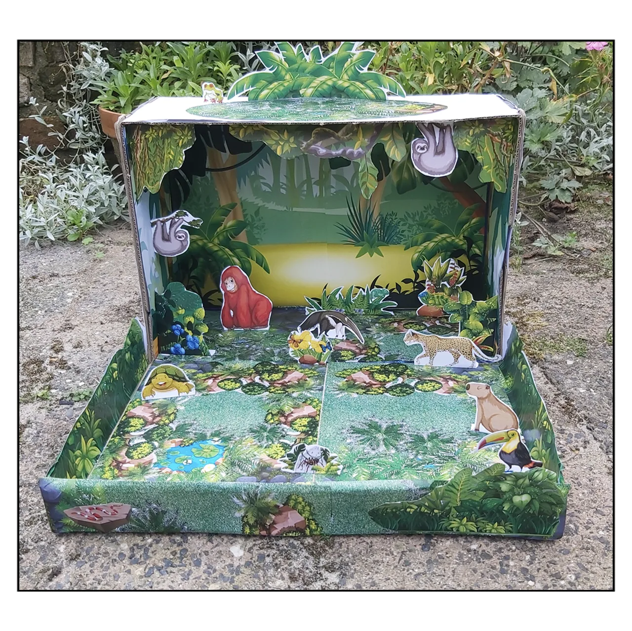 Completed printable Rainforest Habitat shoebox diorama for kids with tropical plants, jungle scenery and rainforest animals